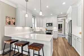 A modern kitchen with white cabinetry, a large island with bar stools, stainless steel appliances, and pendant lighting. - Seabrook Grand Slam | Family, Remote Workspace | 3BR, Sleeps 6, Fernwood (Pacific Beach)