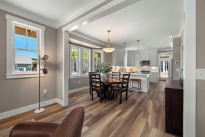 A spacious kitchen with a central island, large windows, and a dining area with a wooden table and chairs.