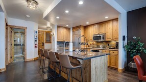 Una cucina moderna con mobili in legno, un frigorifero in acciaio inox, un forno a microonde e un angolo bar con sgabelli.