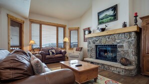 A cozy living room with a stone fireplace, leather sofas, and a view of the city through large windows.