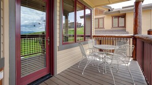 A covered outdoor patio with a table and chairs, large windows, and a view of a green landscape.