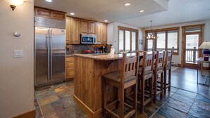 A spacious kitchen with wooden cabinets, a stainless steel refrigerator, a microwave, and a large island with bar stools.