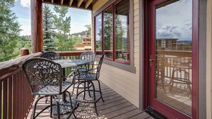 A covered outdoor seating area with metal chairs and a table, overlooking a scenic view of trees and buildings. - AN213 | Antlers Steamboat | Ski In/Out from Patio | Winter Shuttle (Steamboat Springs)