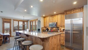 A kitchen with wooden cabinets, a stainless steel refrigerator, a granite countertop, and a bar stool area. - AN213 | Antlers Steamboat | Ski In/Out from Patio | Winter Shuttle (Steamboat Springs)