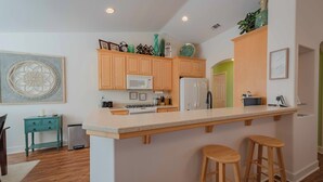 A modern kitchen with wooden cabinets, a large island with stools, a microwave, and a refrigerator.