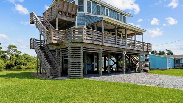 A multi-level wooden house with a balcony, a staircase, and a covered porch area. - Oceanside Home with Hot Tub, Nearby Beach Access, and Grills. A Retreat for All! (Salvo)