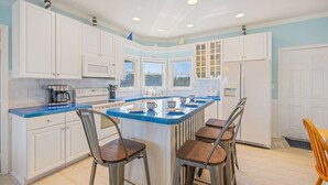 A modern kitchen with white cabinets, a blue countertop, and a central island with stools. - Oceanside Home with Hot Tub, Nearby Beach Access, and Grills. A Retreat for All! (Salvo)