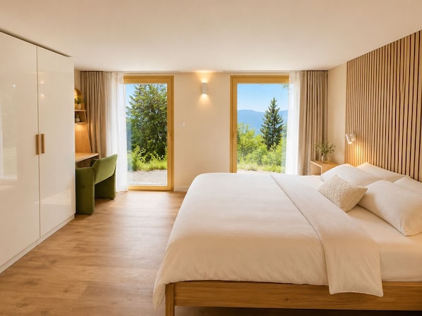 Une chambre moderne avec un grand lit, une armoire en bois, un fauteuil vert et une vue sur la verdure et les montagnes par les fenêtres.