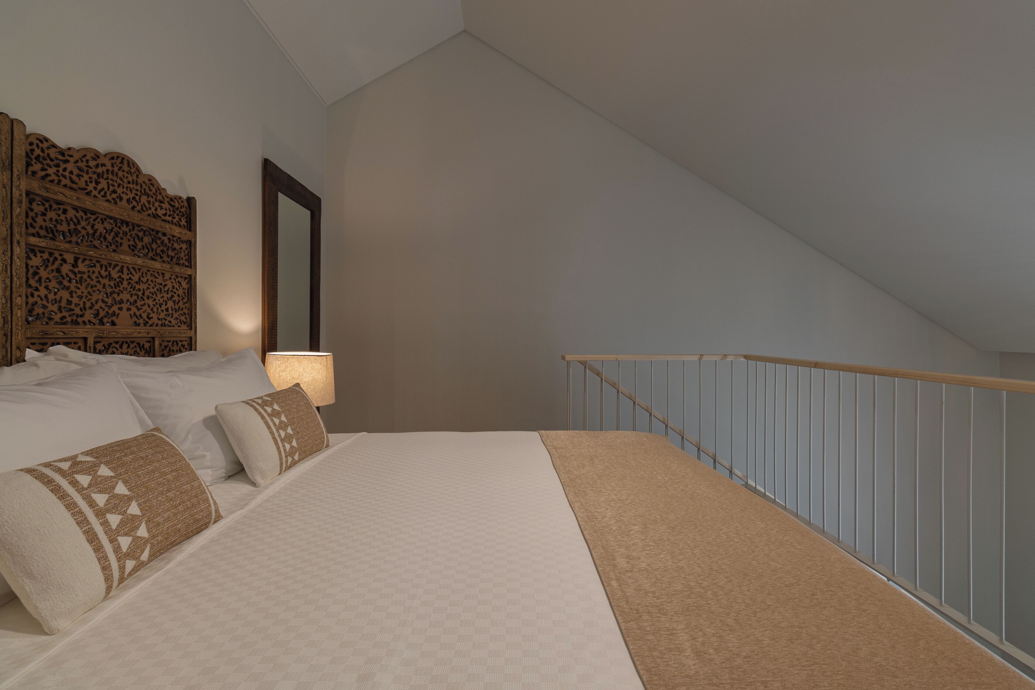 Un dormitorio con una cama grande, cabecera de madera, mesita de noche y un espejo fijado a la pared.