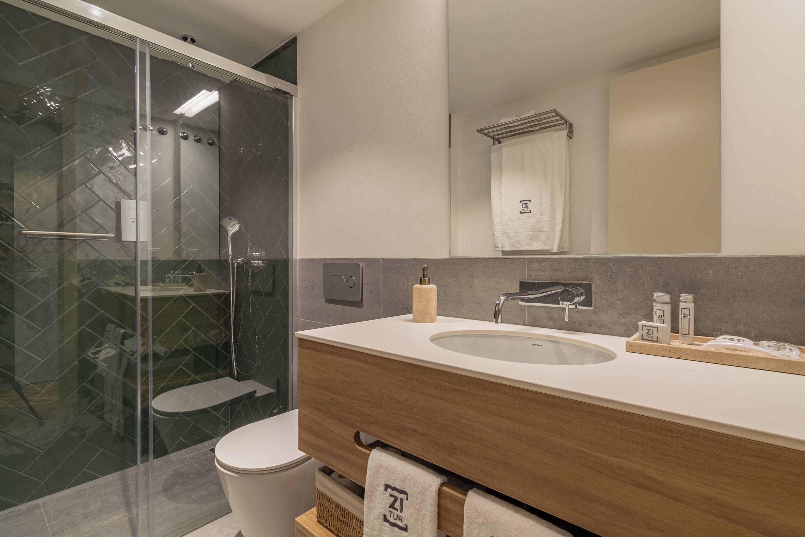 Un baño moderno con ducha envuelta en vidrio, un mueble de tocador de madera con lavabo y un perchero para toallas.