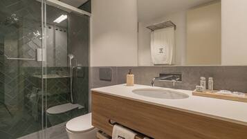 Un baño moderno con ducha envuelta en vidrio, un mueble de tocador de madera con lavabo y un perchero para toallas.
