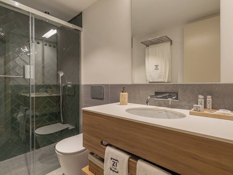 Un baño moderno con ducha envuelta en vidrio, un mueble de tocador de madera con lavabo y un perchero para toallas.