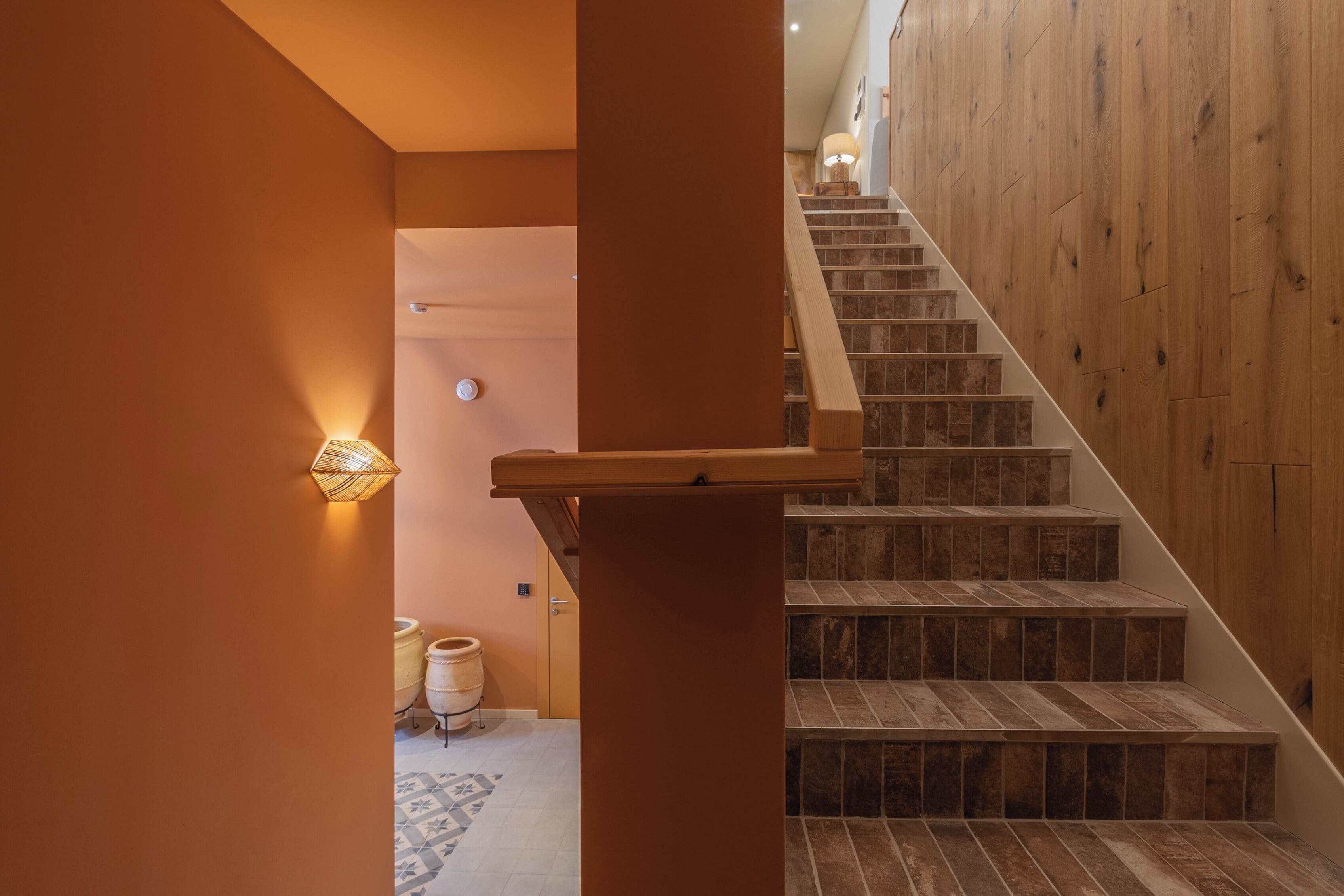 A staircase with wooden steps and a handrail, leading to a room with a door and a light fixture on the wall.