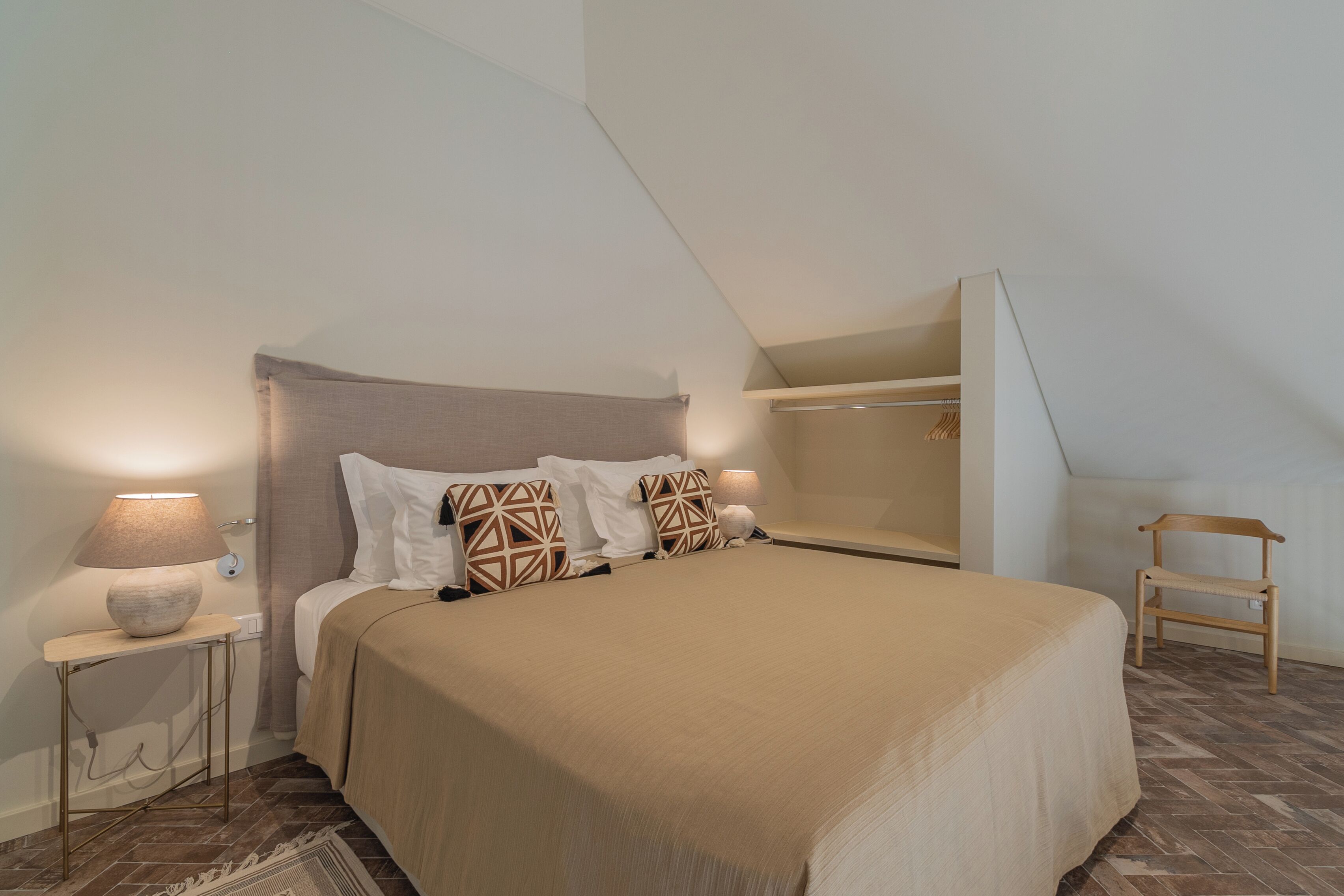 Un dormitorio con cama, mesitas de noche, lámpara, una silla y ventana.