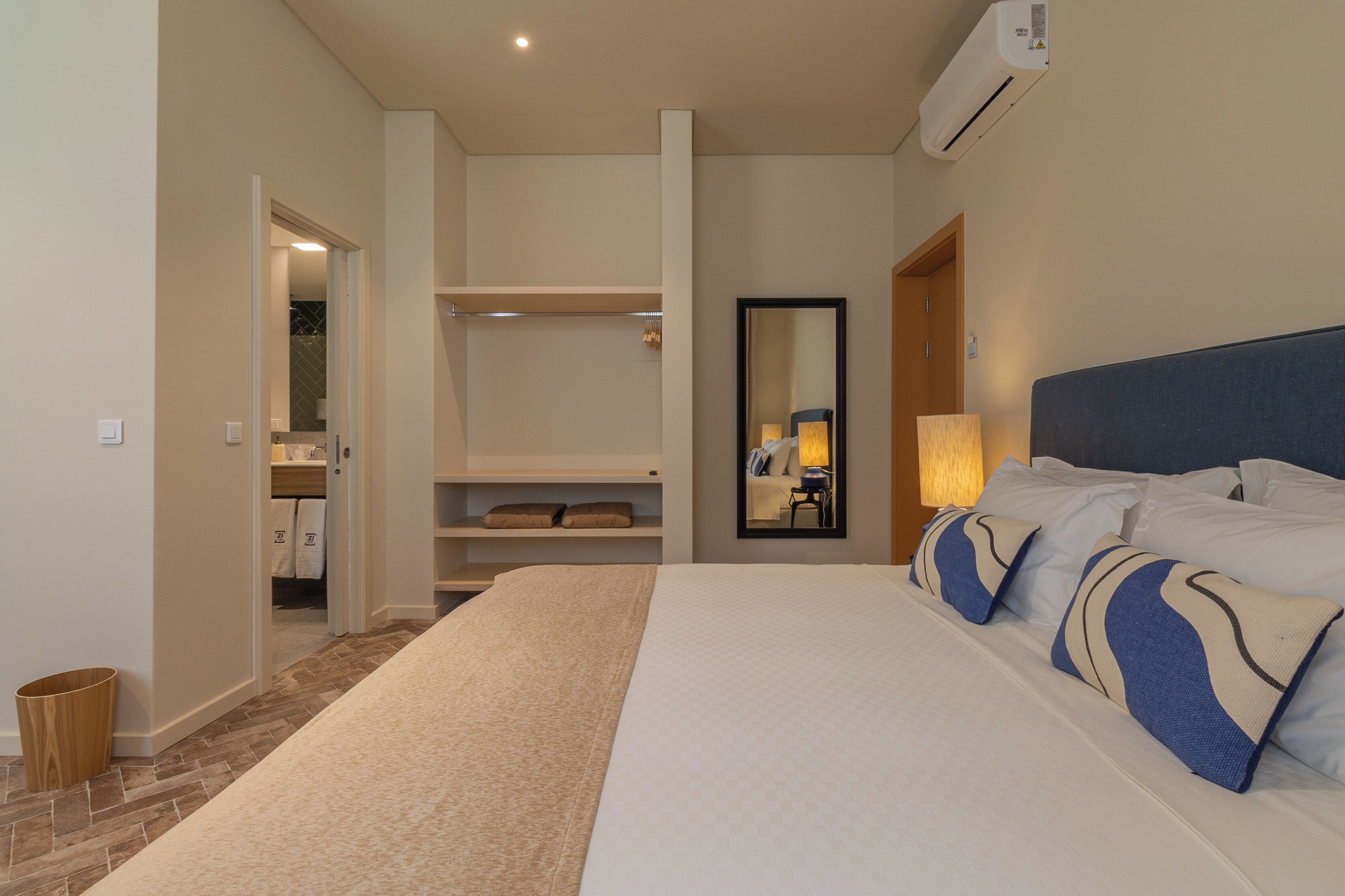 Una camera d'albergo con un letto grande, uno specchio, un armadio e un bagno visibile attraverso una porta aperta.
