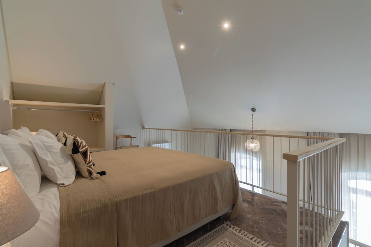 A bedroom with a large bed, a wardrobe, a hanging light fixture, and a view of the outdoors.
