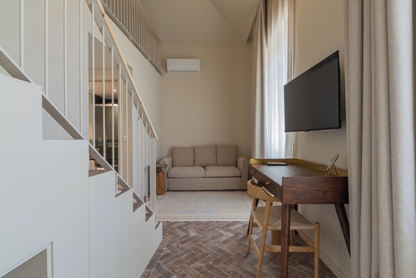 A compact living space with a sofa, a desk, a TV, and a staircase.
