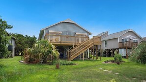 A two-story house with a wooden deck and a staircase leading to a balcony. - The Marsh: Cozy Cottage with Beautiful Marsh Views, Short Walk to Beach (Oak Island)