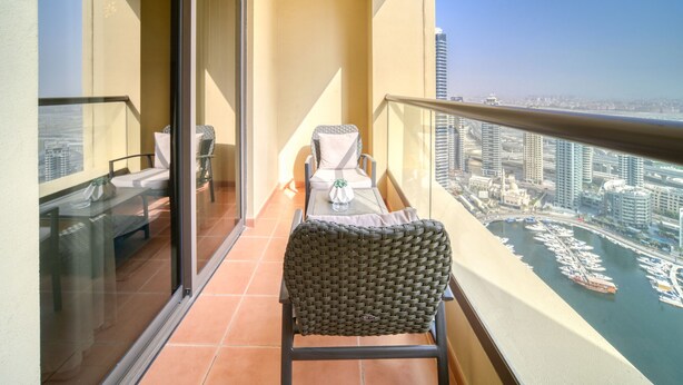 A balcony with a wicker chair, a table with a vase, and a view of a marina with boats and buildings. - High Floor 2BR w/ a View of the Dubai Marina,Near fr. the Beach , Shams 1, JBR (Dubai)