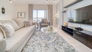 A modern living room with a sofa, a glass coffee table, a TV, and a large window with curtains. - High Floor 2BR w/ a View of the Dubai Marina,Near fr. the Beach , Shams 1, JBR (Dubai)