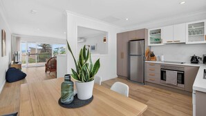 Eine moderne Küche mit weißen Schränken, einem Edelstahlkühlschrank und einem Essbereich mit einem Holztisch und Stühlen.