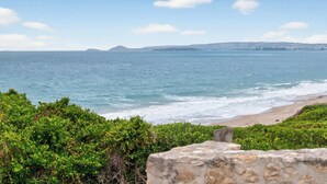 Eine Küstenlandschaft mit klarem Blick auf das Meer, einem Sandstrand und fernen Hügeln.