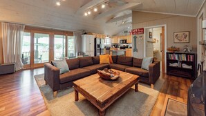 A spacious living room with a large sectional sofa, a wooden coffee table, and a kitchen in the background. - Dog Friendly Cottage w/ Dock & Shuffleboard (Swanton)