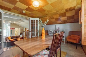 Ein Essbereich mit einem Holztisch, Stühlen und einer Blumenvase. Im Hintergrund befinden sich eine Couch und ein Sessel.