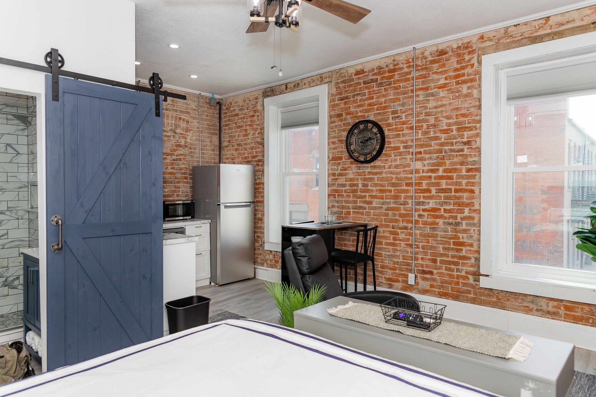 A modern kitchen with a brick wall, a blue door, and a dining area with a table and chairs.