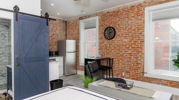 A modern kitchen with a brick wall, a blue door, and a dining area with a table and chairs.