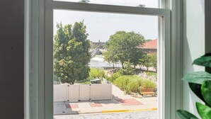 A view through a window of a street with trees, a bench, and a building with a red roof.