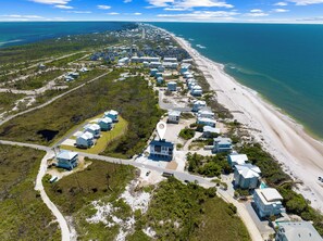 An aerial view of a coastal residential area with houses along the beach, a clear sky, and the ocean in the background.