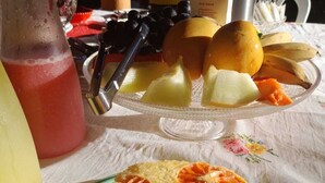 Une table mise pour le petit-déjeuner avec une assiette de fruits, un verre de jus et une machine à café.