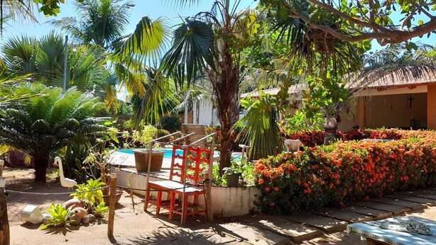 Un jardin tropical avec une piscine, des chaises rouges et un bâtiment au toit de chaume.