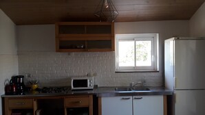 A kitchen with a white brick wall, wooden cabinets, a microwave, a sink, and a refrigerator. - Maison au Calme Avec Jardin, Terrasse et Barbecue (Dampierre-sur-Boutonne)