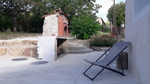 A brick oven structure with steps leading up to it, surrounded by gravel and greenery. - Maison au Calme Avec Jardin, Terrasse et Barbecue (Dampierre-sur-Boutonne)