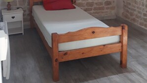 A bedroom with a wooden bed, a red pillow, a nightstand, and a stone wall. - Maison au Calme Avec Jardin, Terrasse et Barbecue (Dampierre-sur-Boutonne)