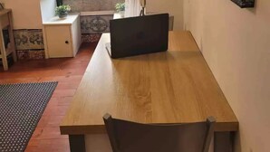 Une pièce comprenant une table en bois, une chaise, une petite table d’appoint avec une plante, une fenêtre avec des rideaux et un tableau accroché au mur.