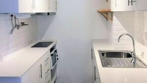 Une cuisine compacte avec des meubles blancs, un four encastré, un évier et un luminaire fixé au plafond.
