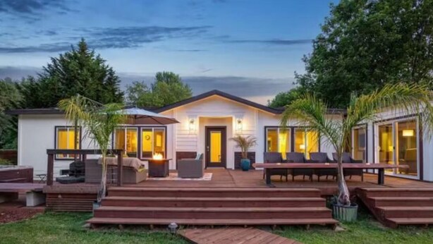 Ein modernes Haus mit Terrasse, Sitzgelegenheiten im Freien und einem gut beleuchteten Eingang.