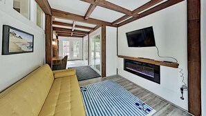 Ein modernes Wohnzimmer mit einem gelben Sofa, einem Kamin, einem Wand-Fernseher und Holzbalken an der Decke.