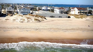 Uma área residencial costeira com casas perto da praia, céu claro e vista para o oceano.
