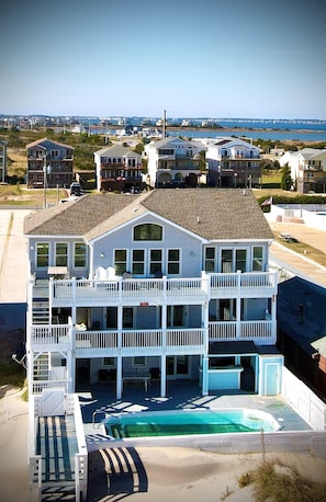 A two-story beachfront house with a swimming pool, multiple balconies, and a view of the ocean and other houses.