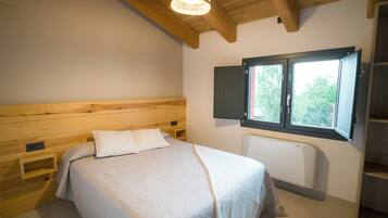 A bedroom with a wooden headboard, a bed with white bedding, a window with a view of greenery, and a built-in heater.