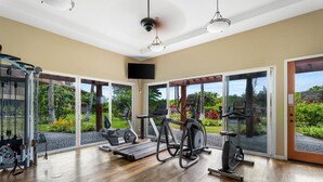 A spacious gym with cardio machines, free weights, and a large window offering a view of a landscaped garden.