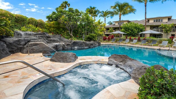 A hot tub surrounded by a pool, with a rocky edge and lounge chairs.