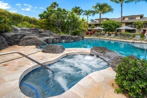 A hot tub surrounded by a pool, with a rocky edge and lounge chairs.