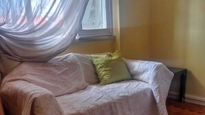 A room with a sofa, a green pillow, a small table, and a window with curtains. - Room for Rent in Almada/lisbon (Almada)