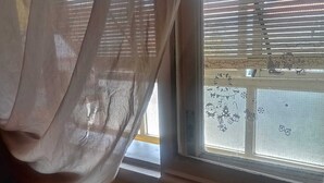 A bedroom with a bed, a window with blinds, and a view of the street outside. - Room for Rent in Almada/lisbon (Almada)