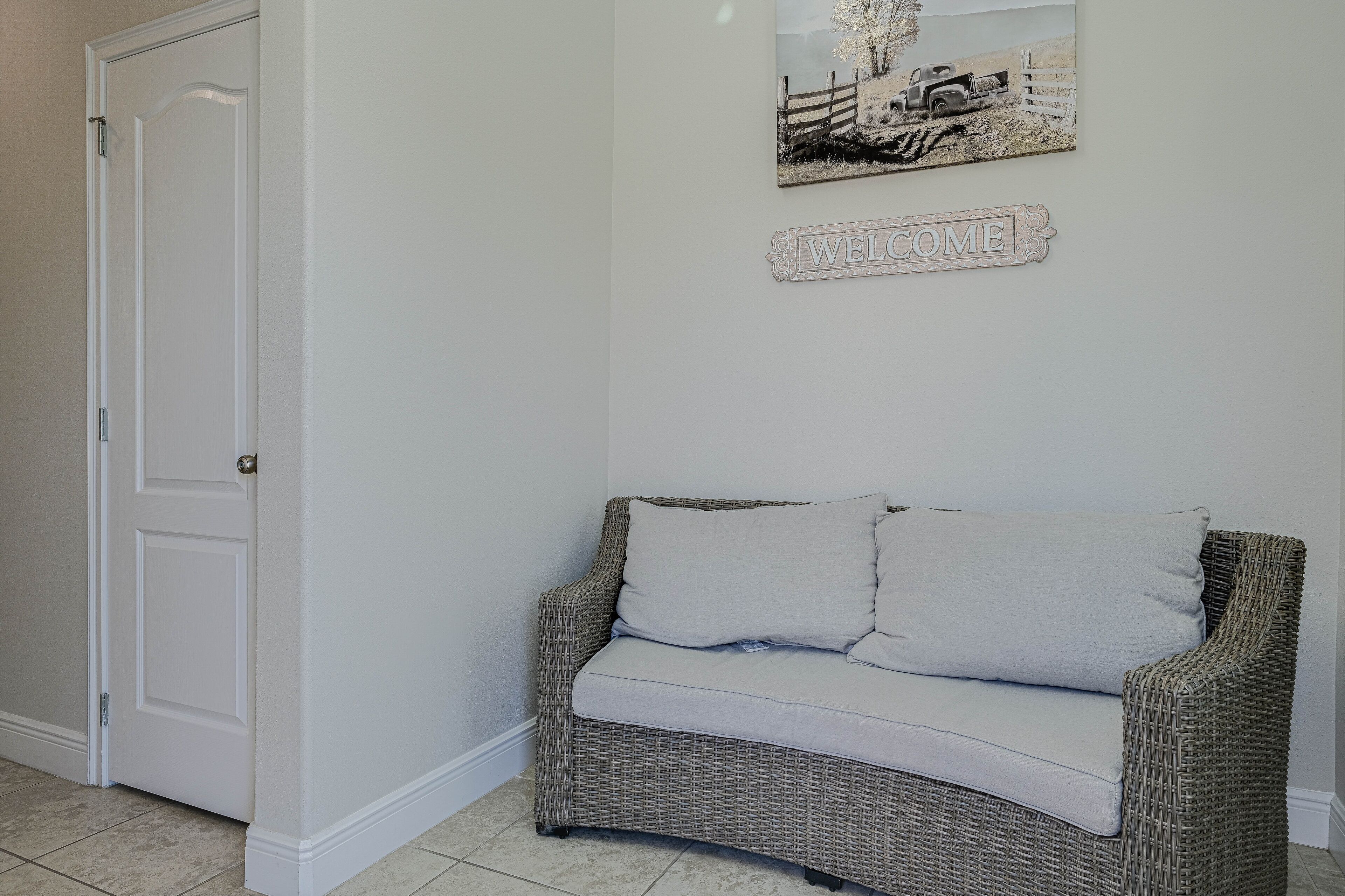 A room with a white door, a wicker sofa with two pillows, and a welcome sign on the wall.